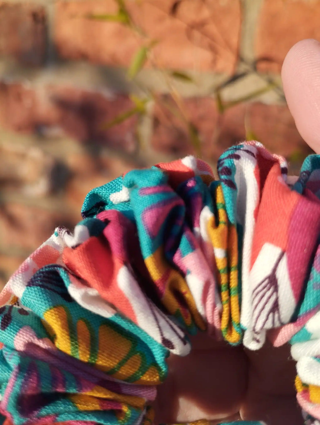Close-up of the teal, pink, red, yellow and cream cotton fabric on Carnival Bloom Medium scrunchie