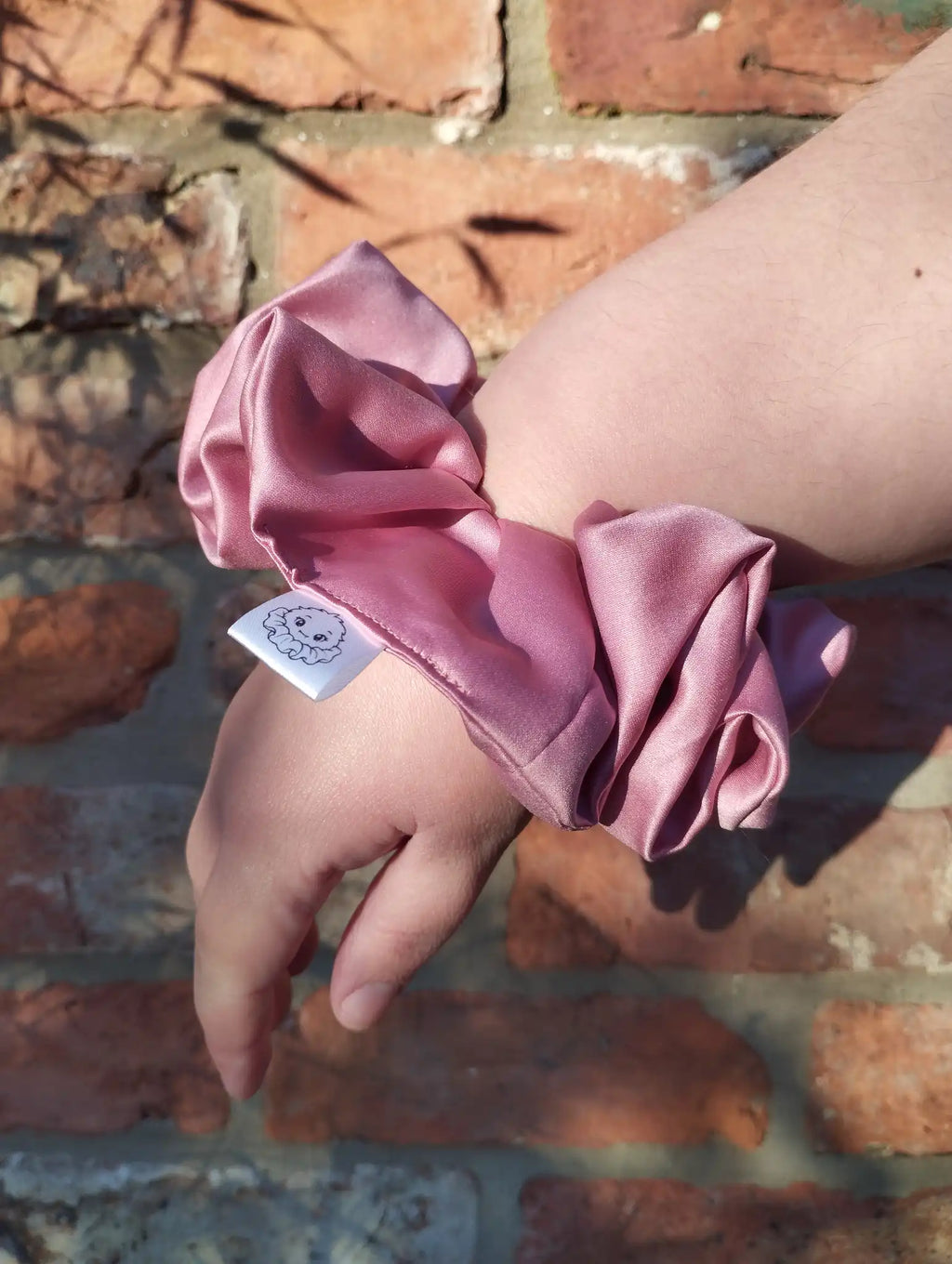 Dusky Rose satin Jumbo scrunchie worn on a wrist to show its size