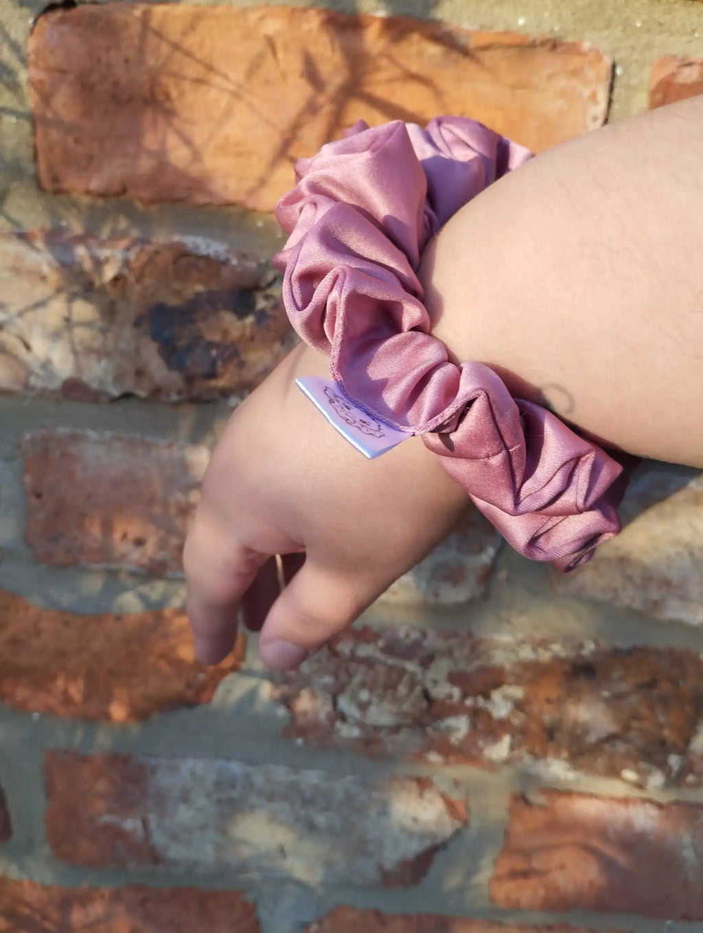 Dusky Rose satin Medium scrunchie worn on a wrist to show its size