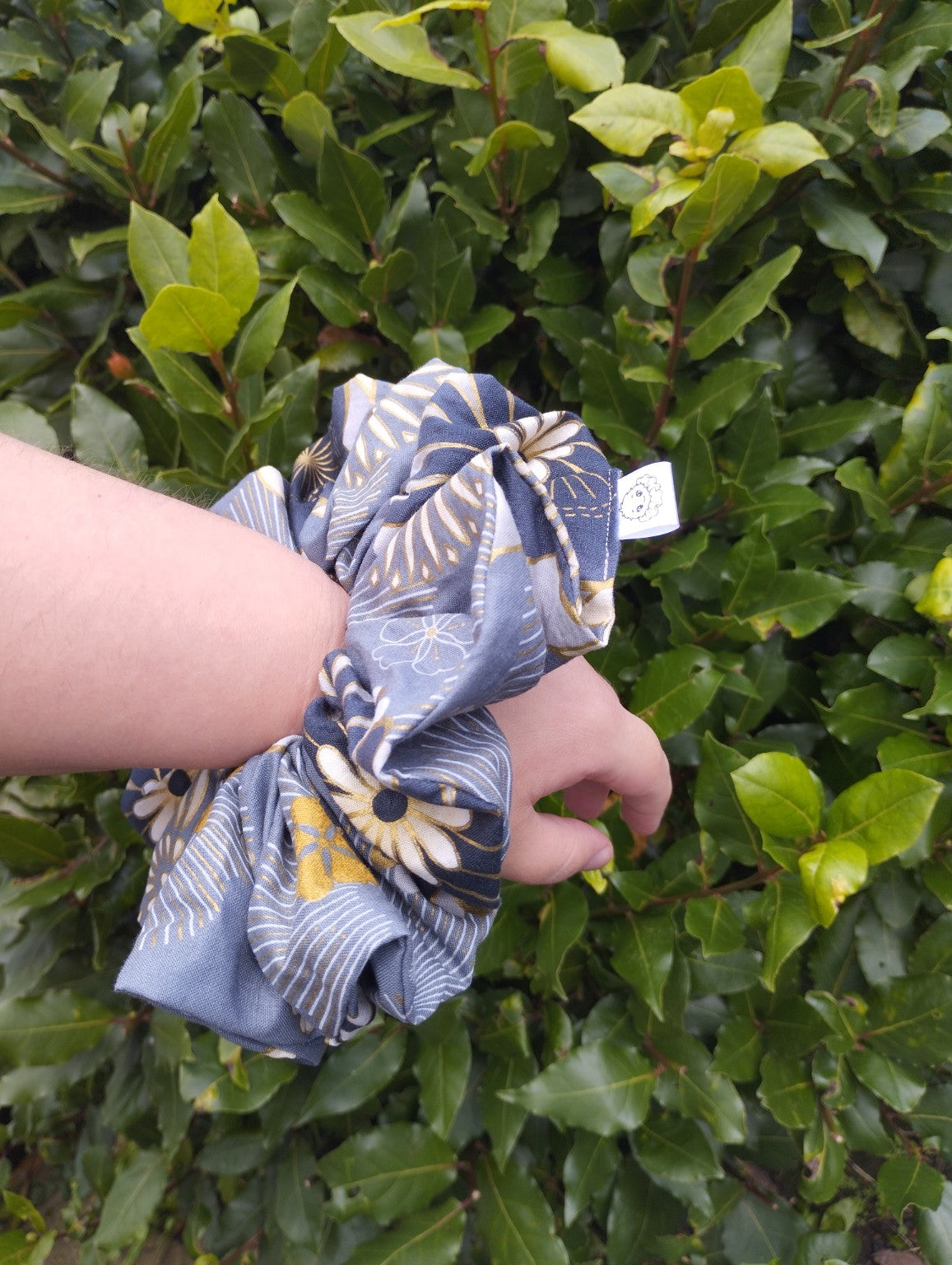 Golden Meadow oversized blue-grey floral scrunchie worn on a wrist to show its size